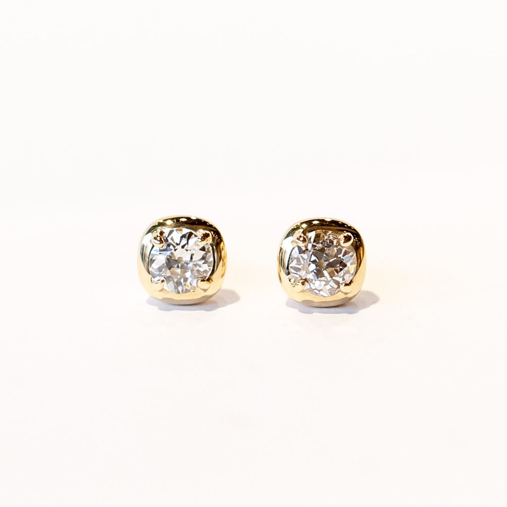 Old mine cut diamonds are prong set into a squared cushion-shaped yellow gold setting in these diamond stud earrings.
