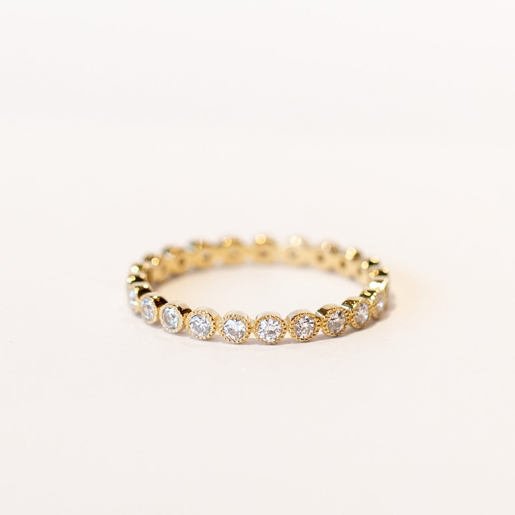 A yellow gold diamond eternity band with round white diamonds set in bezels with milgrain edges.