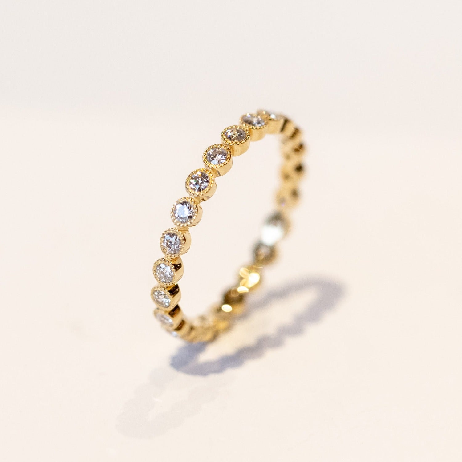 A yellow gold diamond eternity band with round white diamonds set in bezels with milgrain edges.