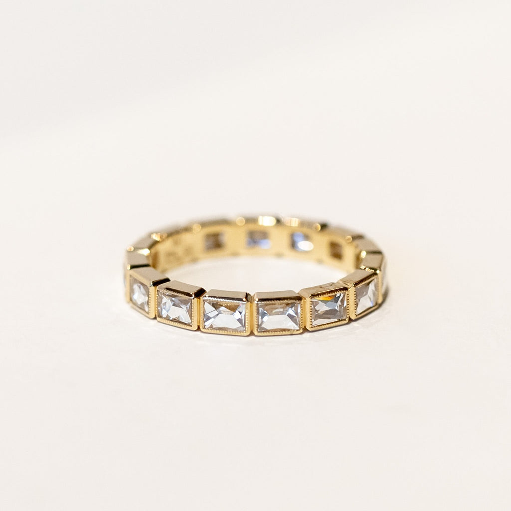 A yellow gold diamond eternity band set with bezel-set french cut diamonds and milgrain edges.