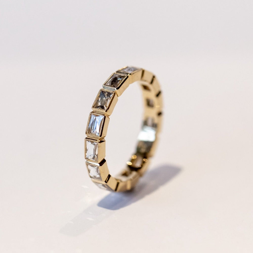 A yellow gold diamond eternity band set with bezel-set french cut diamonds and milgrain edges.