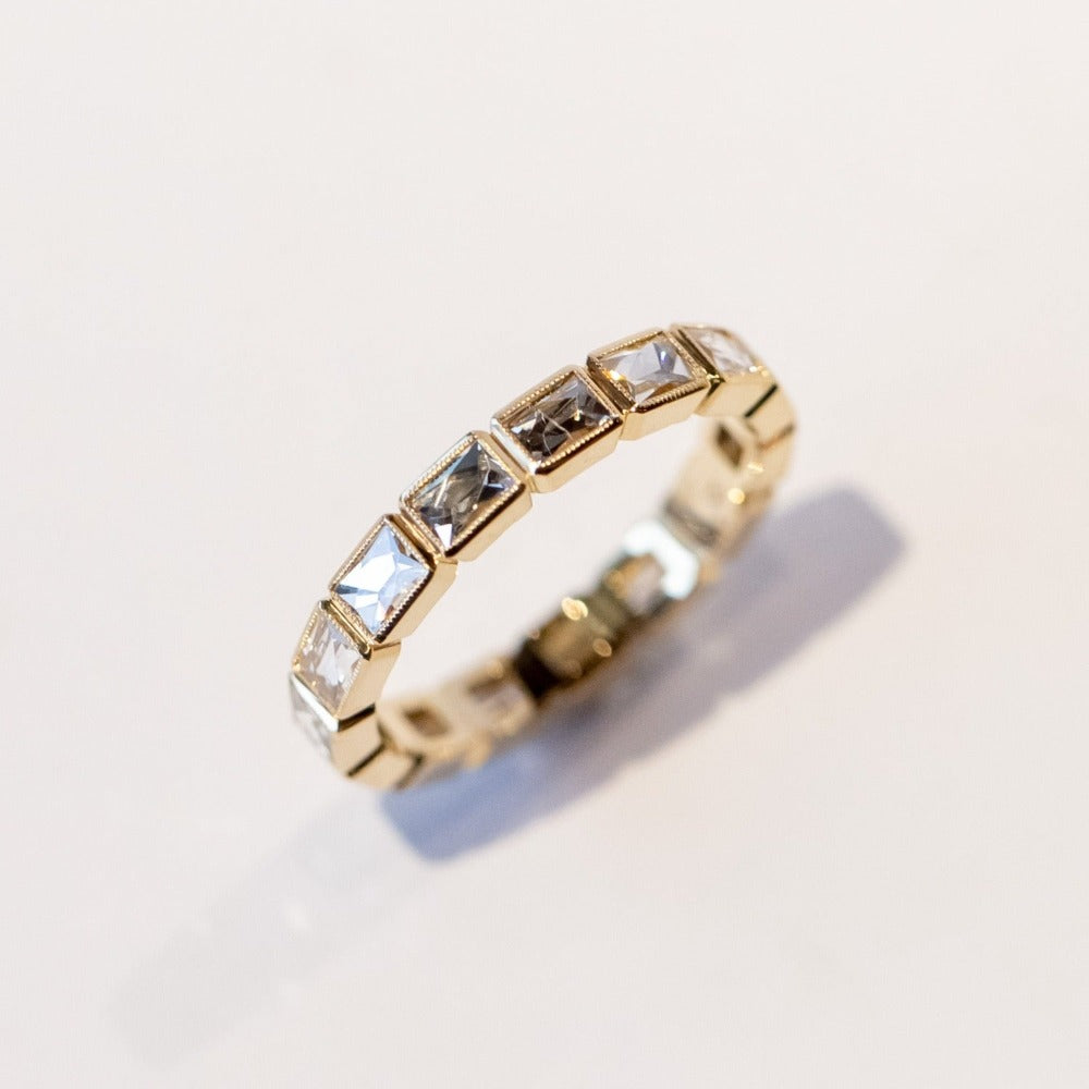 A yellow gold diamond eternity band set with bezel-set french cut diamonds and milgrain edges.