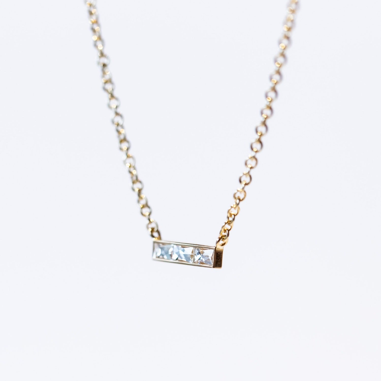 A bar-style diamond station necklace set with three rectangular French cut diamonds in a horizontal bar with a classic yellow gold cable chain.