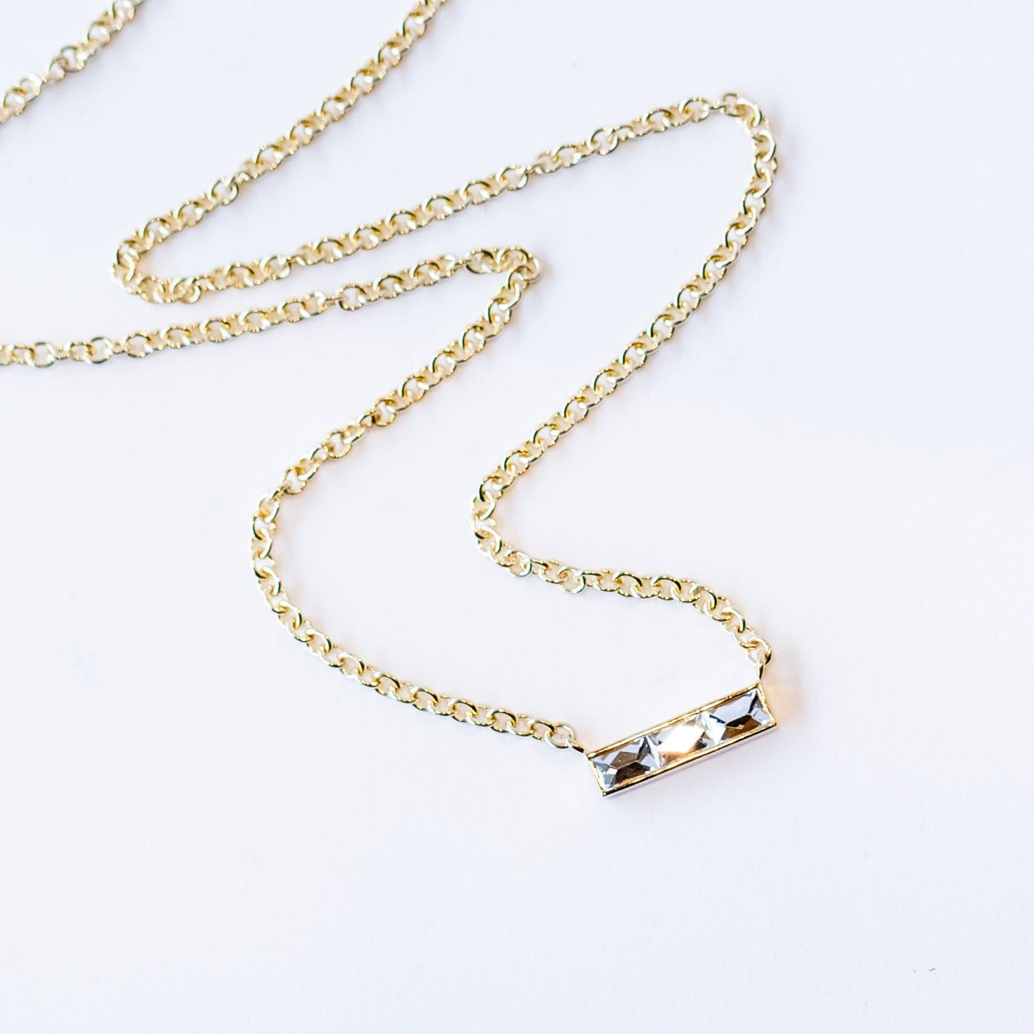A bar-style diamond station necklace set with three rectangular French cut diamonds in a horizontal bar with a classic yellow gold cable chain.