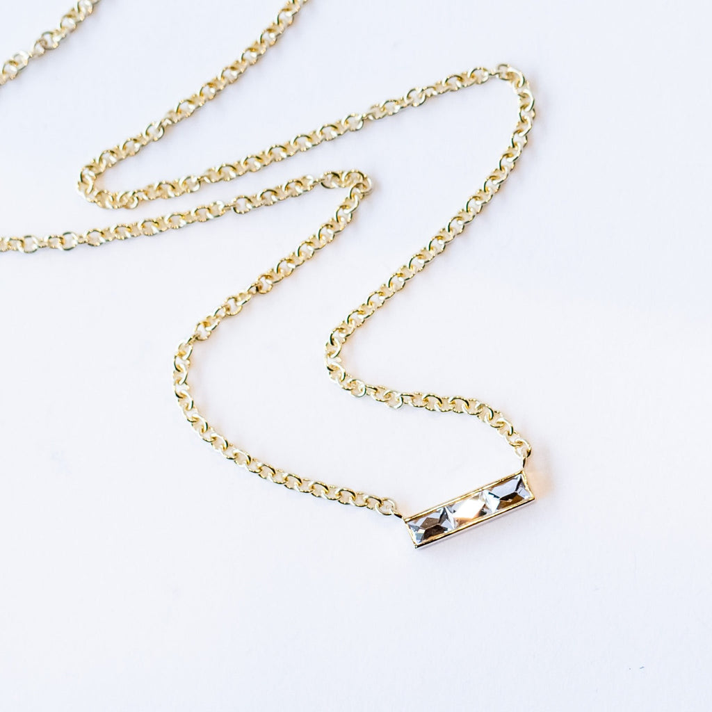 A bar-style diamond station necklace set with three rectangular French cut diamonds in a horizontal bar with a classic yellow gold cable chain.