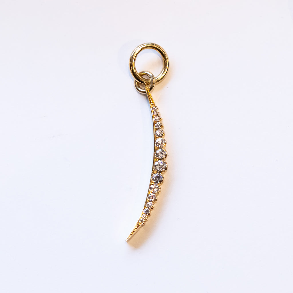 A slim, elongated crescent moon charm in yellow gold, set with a row of pave diamonds. 