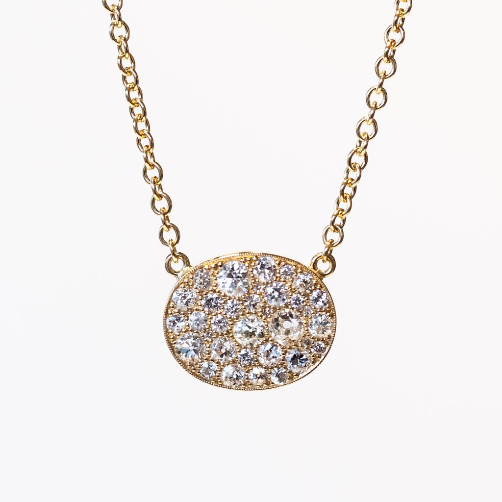 A yellow gold chain necklace featuring a horizontal oval plate at the center set with a cobblestone pattern of different size round pave diamonds.