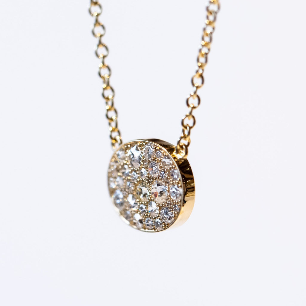 A yellow gold chain necklace featuring a horizontal oval plate at the center set with a cobblestone pattern of different size round pave diamonds.