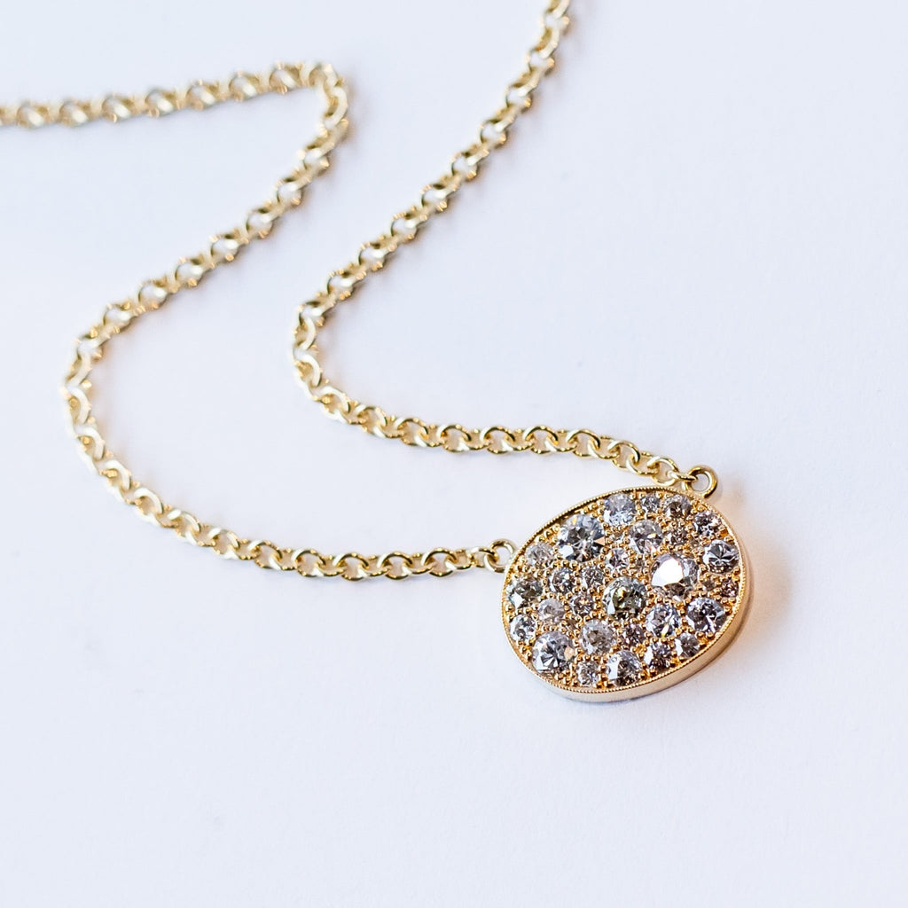 A yellow gold chain necklace featuring a horizontal oval plate at the center set with a cobblestone pattern of different size round pave diamonds.