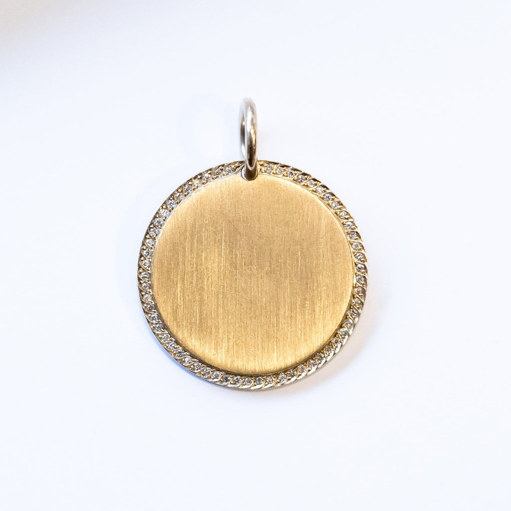 A yellow gold, round disc charm with a ring of diamonds around the outer edge and a brushed matte finish.