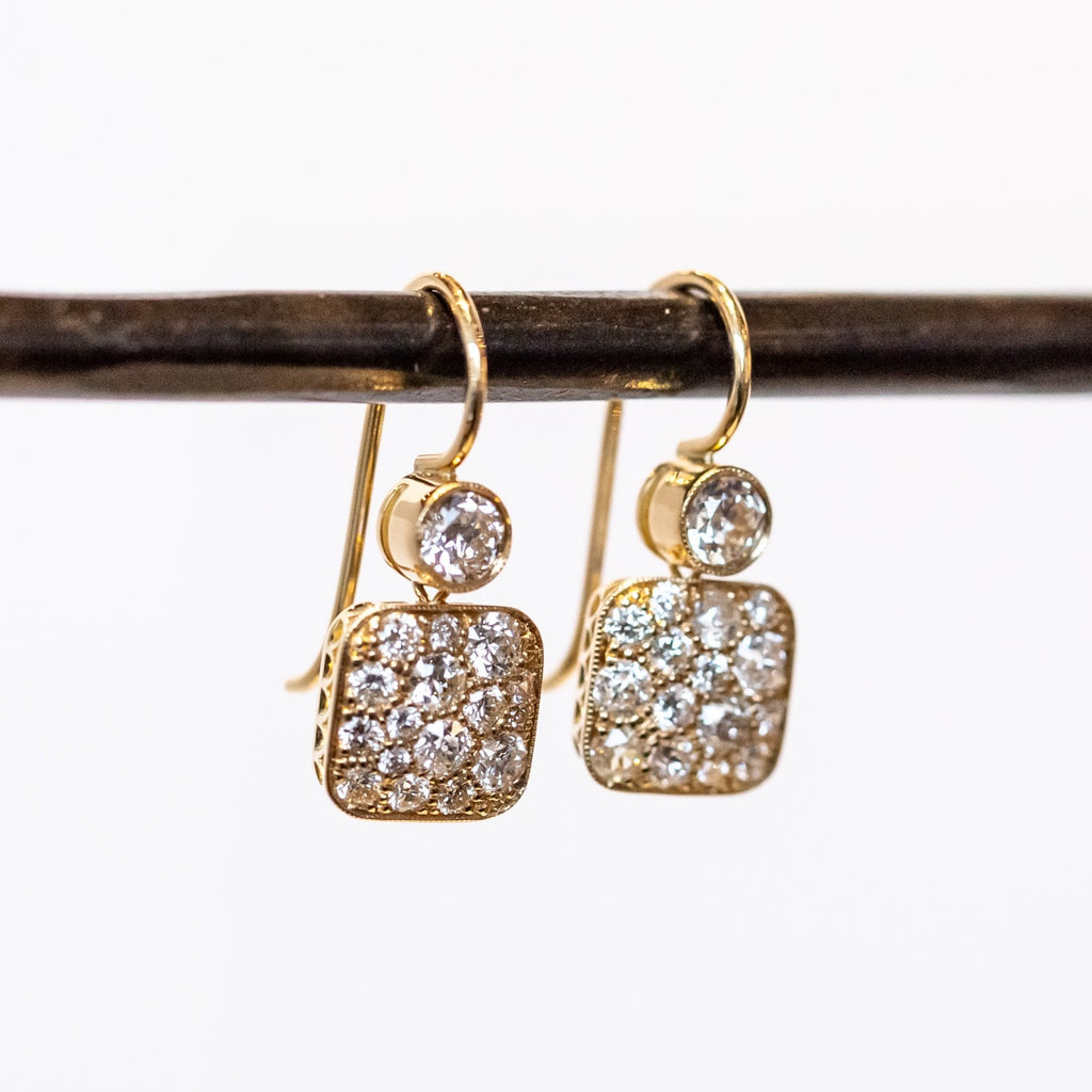 Yellow gold diamond drop earrings featuring a rounded square drop below a small circle. The top circle features one bezel set diamond while the square is covered in cobblestone pave diamonds.