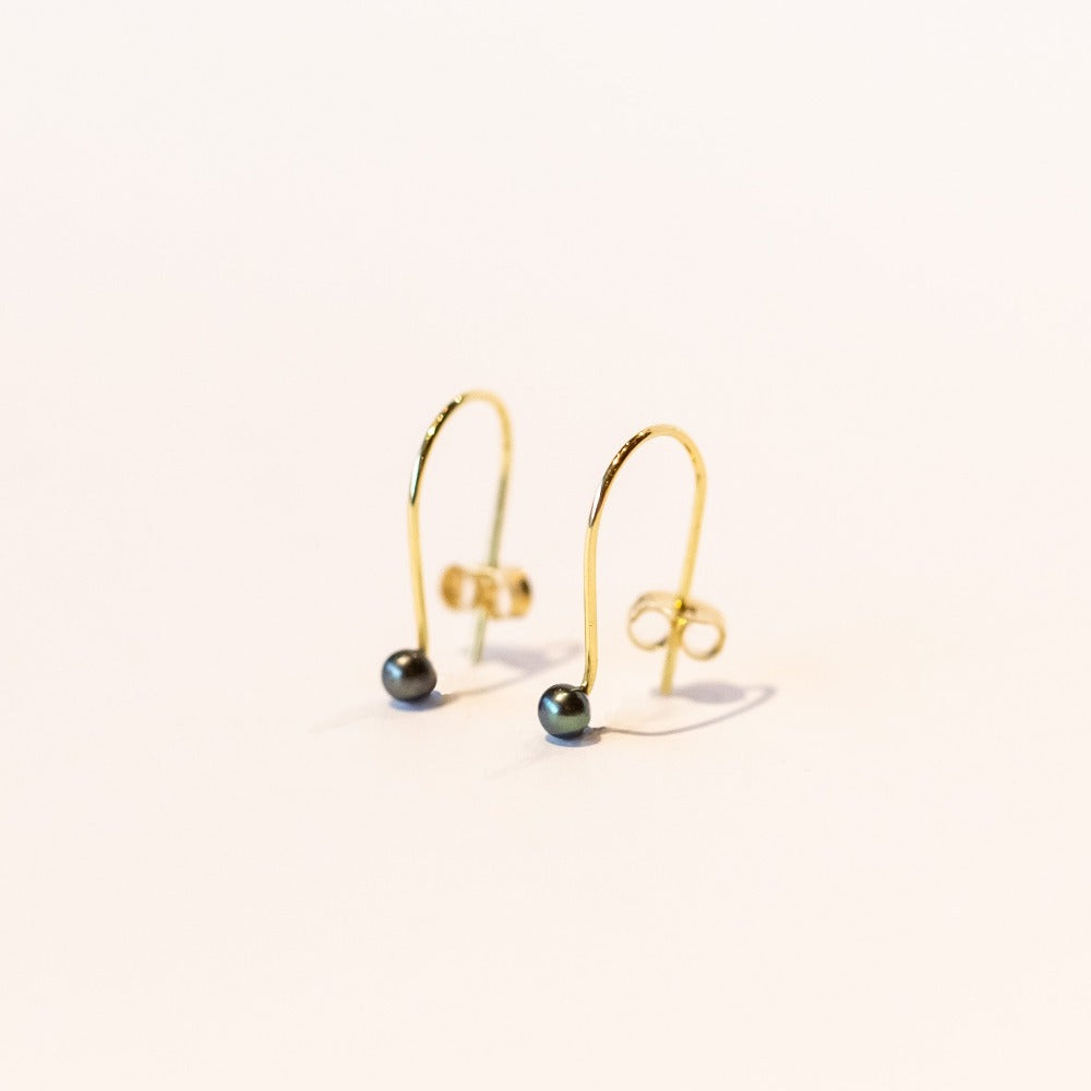 Dainty gold wire hook earrings with tiny black pearls at the end.