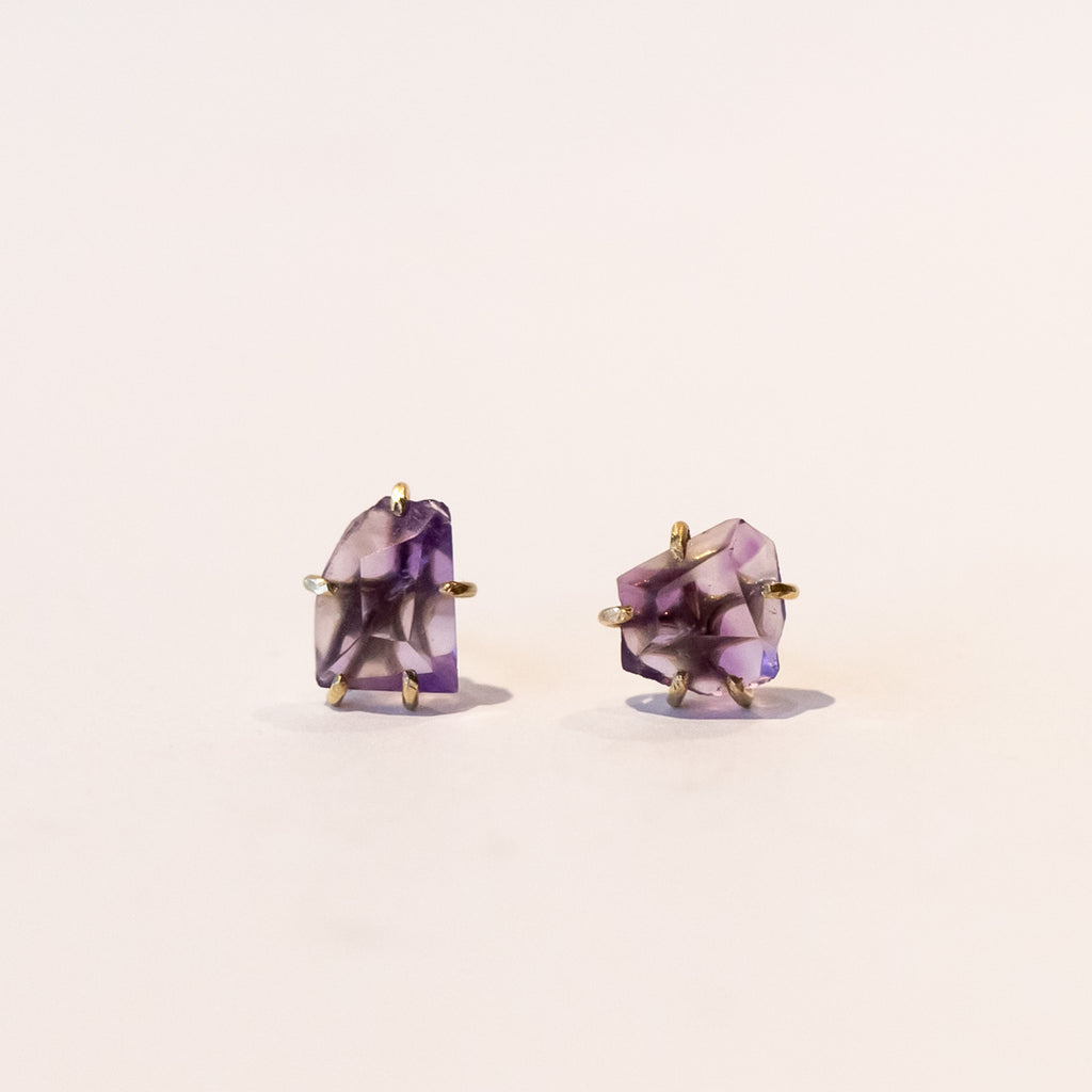 Small roughly faceted amethyst gemstone stud earrings in yellow gold prongs.