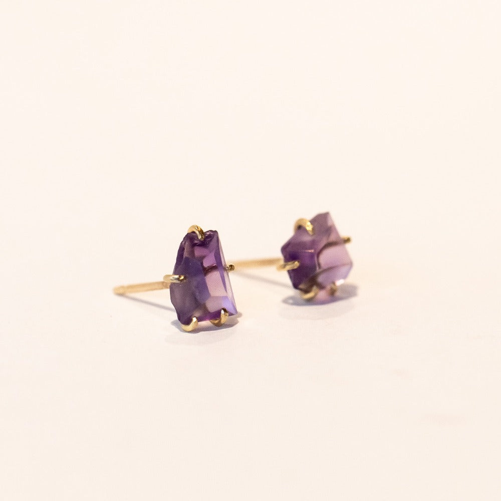 Small roughly faceted amethyst gemstone stud earrings in yellow gold prongs.