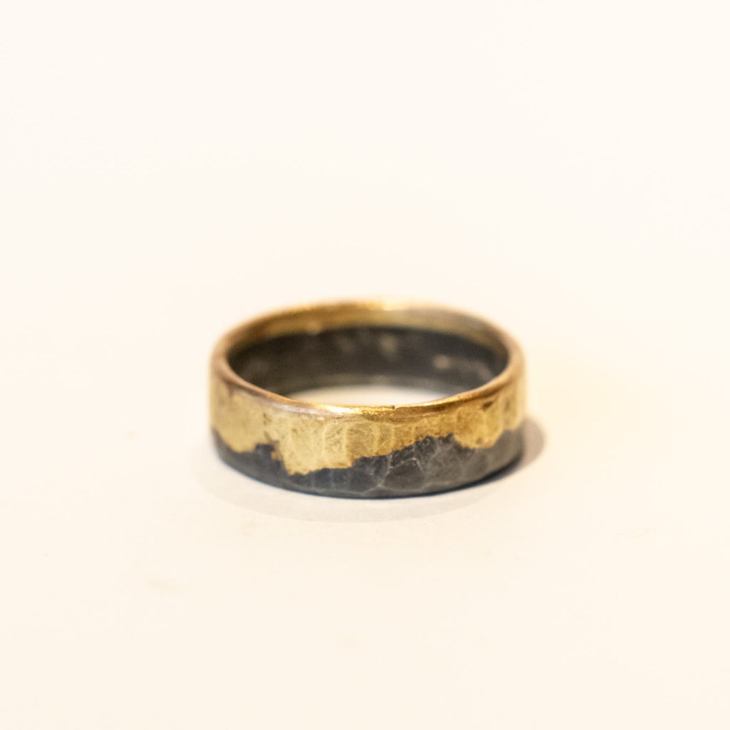 An organic wide wedding band made of melded yellow gold and blackened sterling silver.