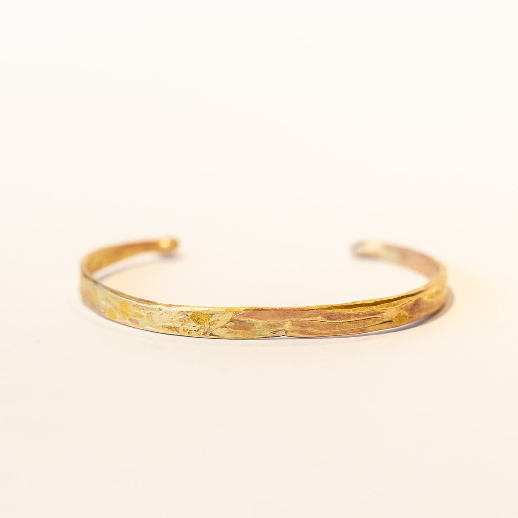 A thin, flat gold cuff bracelet with organic texture.