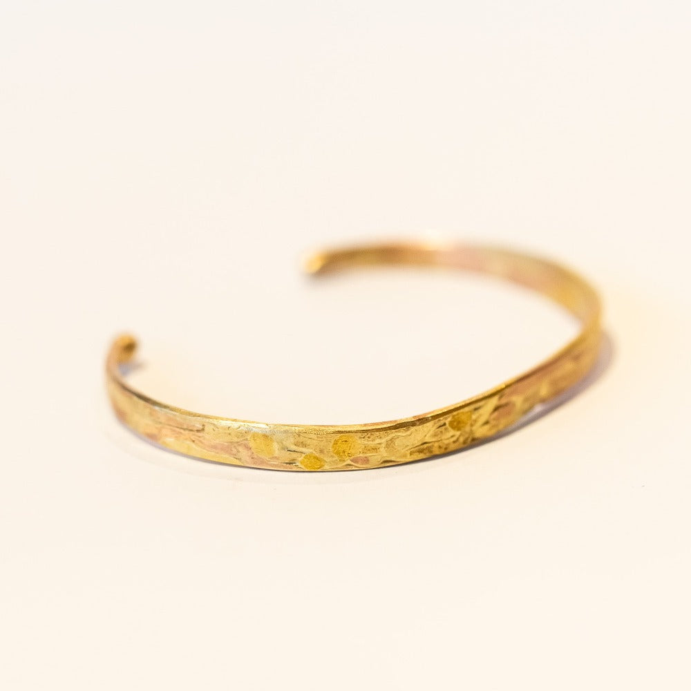 A thin, flat gold cuff bracelet with organic texture.