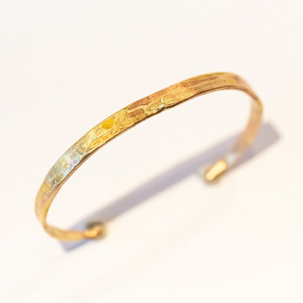 A thin, flat gold cuff bracelet with organic texture.