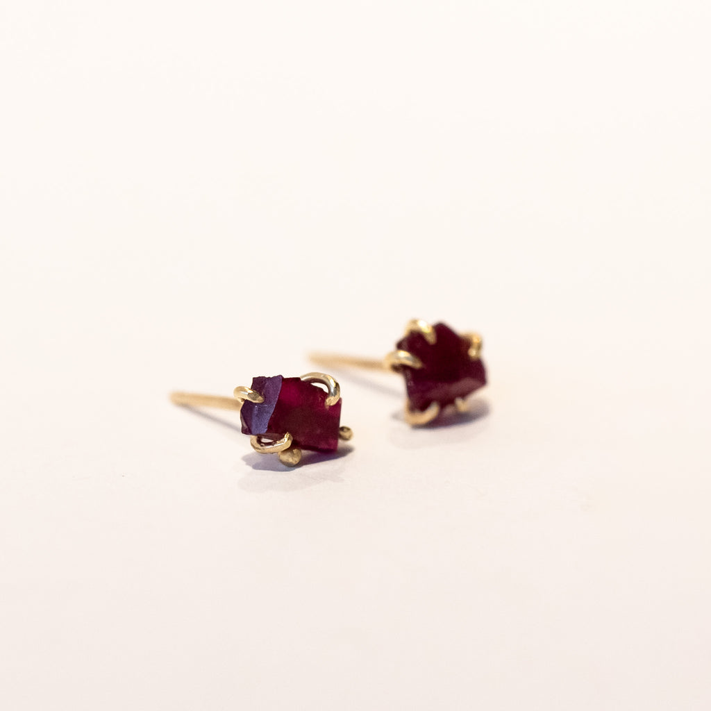 Small, asymmetrical rough faceted ruby stud earrings in yellow gold.
