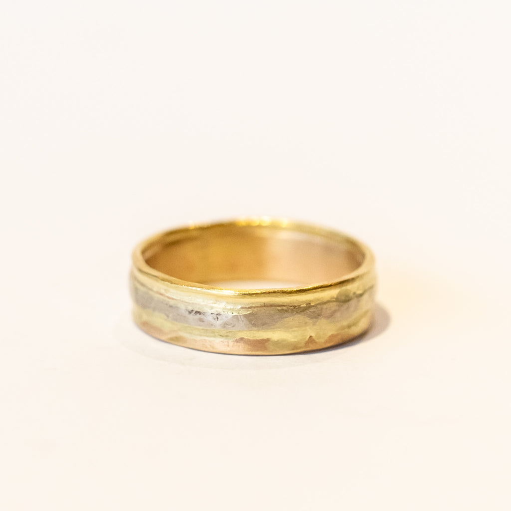 A wide yellow gold wedding band with different karats of gold melded together in linear fashion.