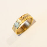 A wide yellow gold wedding band with different karats of gold melded together in linear fashion.