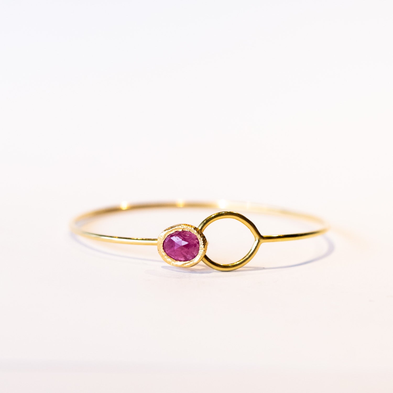 A yellow gold wire bracelet set with a bezel set ruby at one end that fits through a loop at the other.