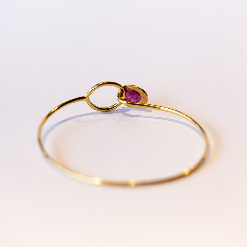 A yellow gold wire bracelet set with a bezel set ruby at one end that fits through a loop at the other.