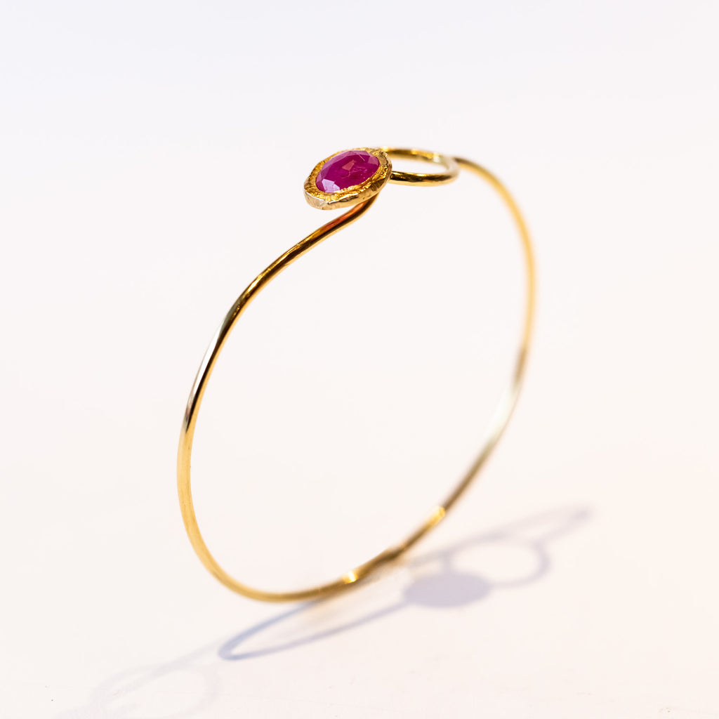 A yellow gold wire bracelet set with a bezel set ruby at one end that fits through a loop at the other.