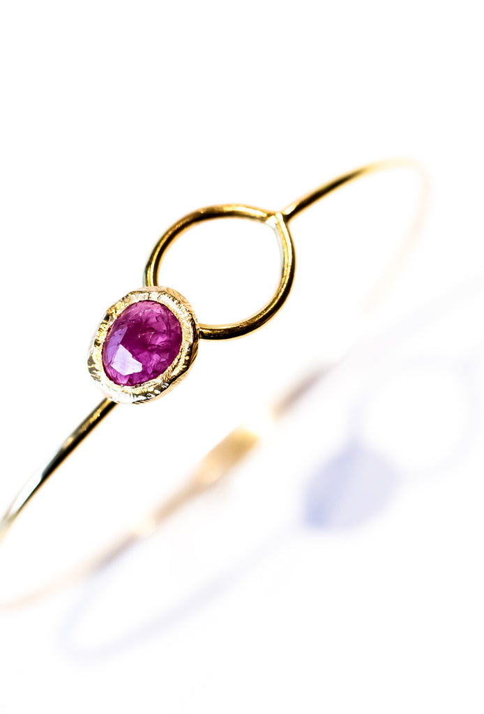 A yellow gold wire bracelet set with a bezel set ruby at one end that fits through a loop at the other.