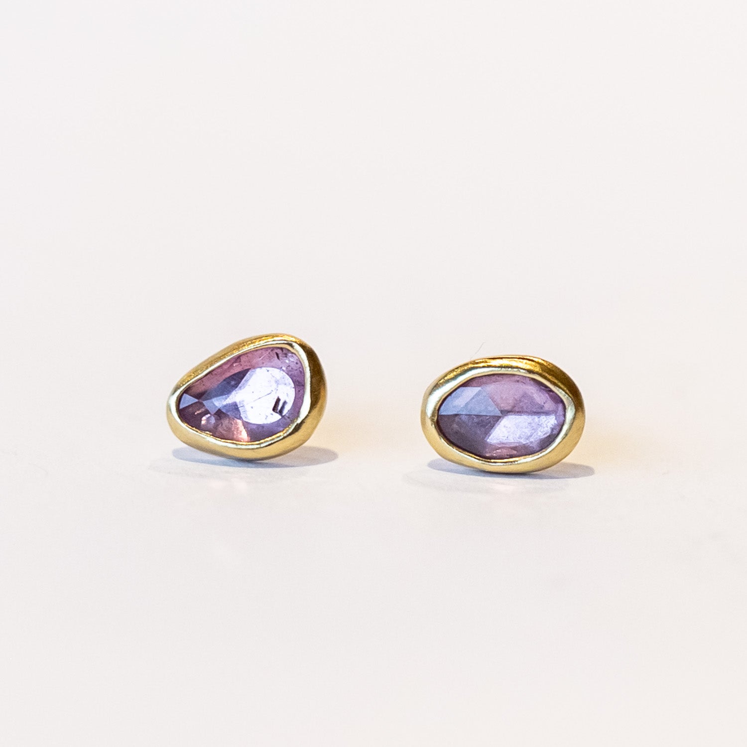 A pair of asymmetrical pink sapphire stud earrings set in yellow gold bezels.