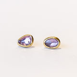 A pair of asymmetrical pink sapphire stud earrings set in yellow gold bezels.