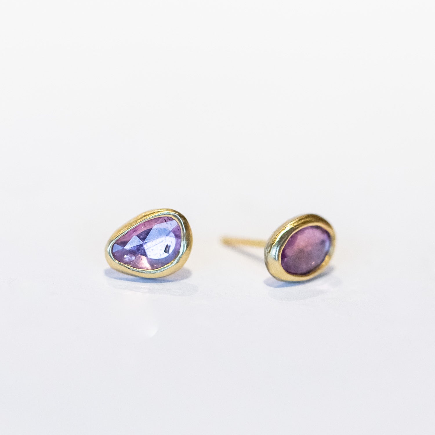 A pair of asymmetrical pink sapphire stud earrings set in yellow gold bezels.