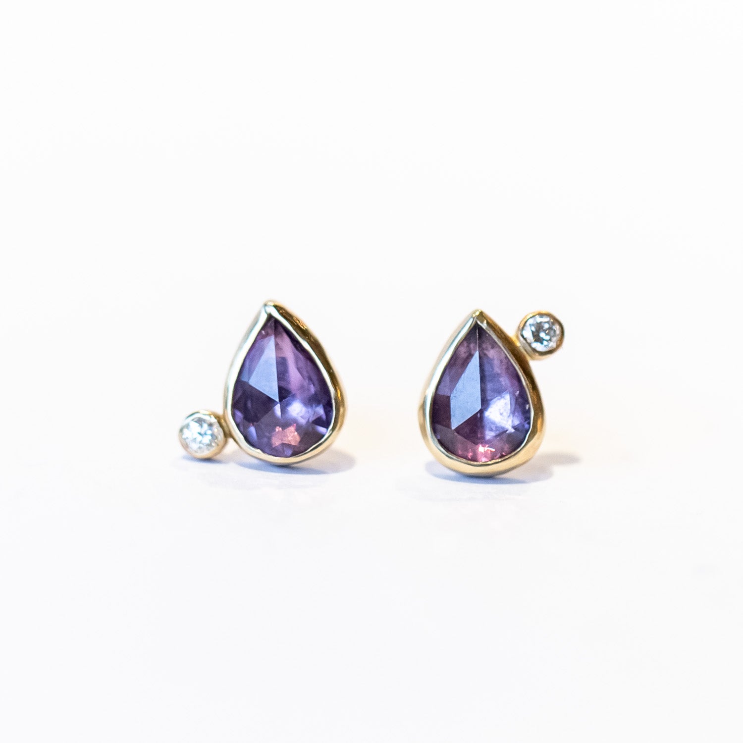 Pear shape purple sapphire stud earrings bezel set in yellow gold and accented by tiny round diamonds.