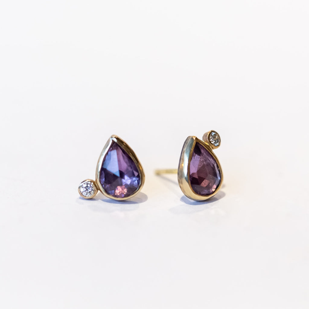 Pear shape purple sapphire stud earrings bezel set in yellow gold and accented by tiny round diamonds.