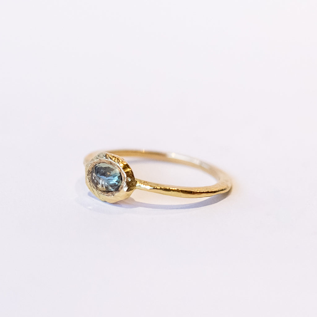 An oval rose cut green sapphire is bezel set into a textured yellow gold ring.