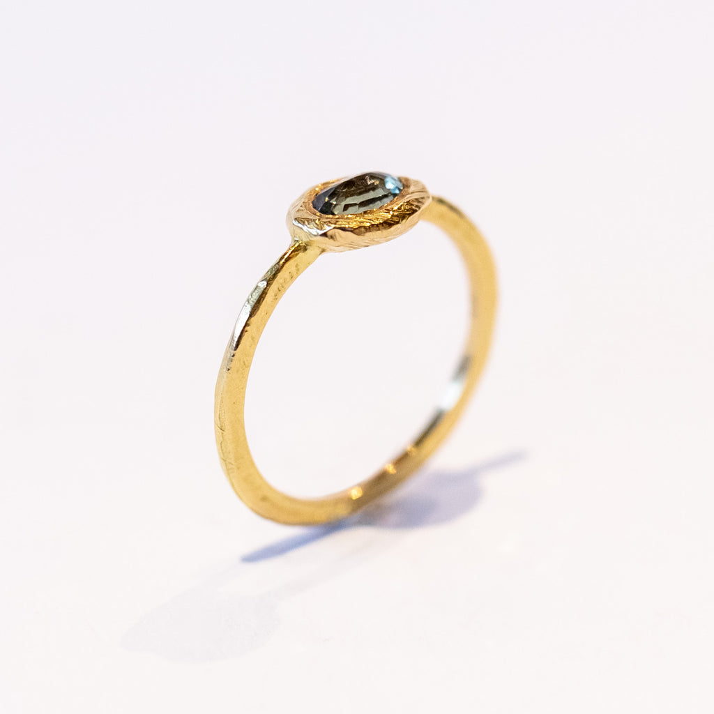 An oval rose cut green sapphire is bezel set into a textured yellow gold ring.
