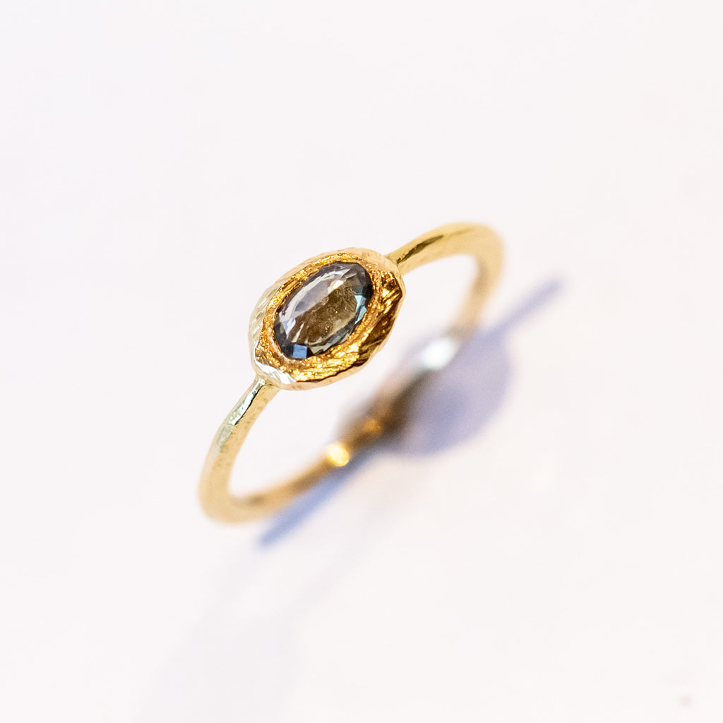 An oval rose cut green sapphire is bezel set into a textured yellow gold ring.