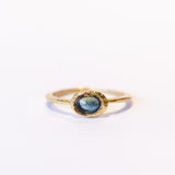 A slender, textured yellow gold ring with an east-west, bezel set teal blue sapphire.