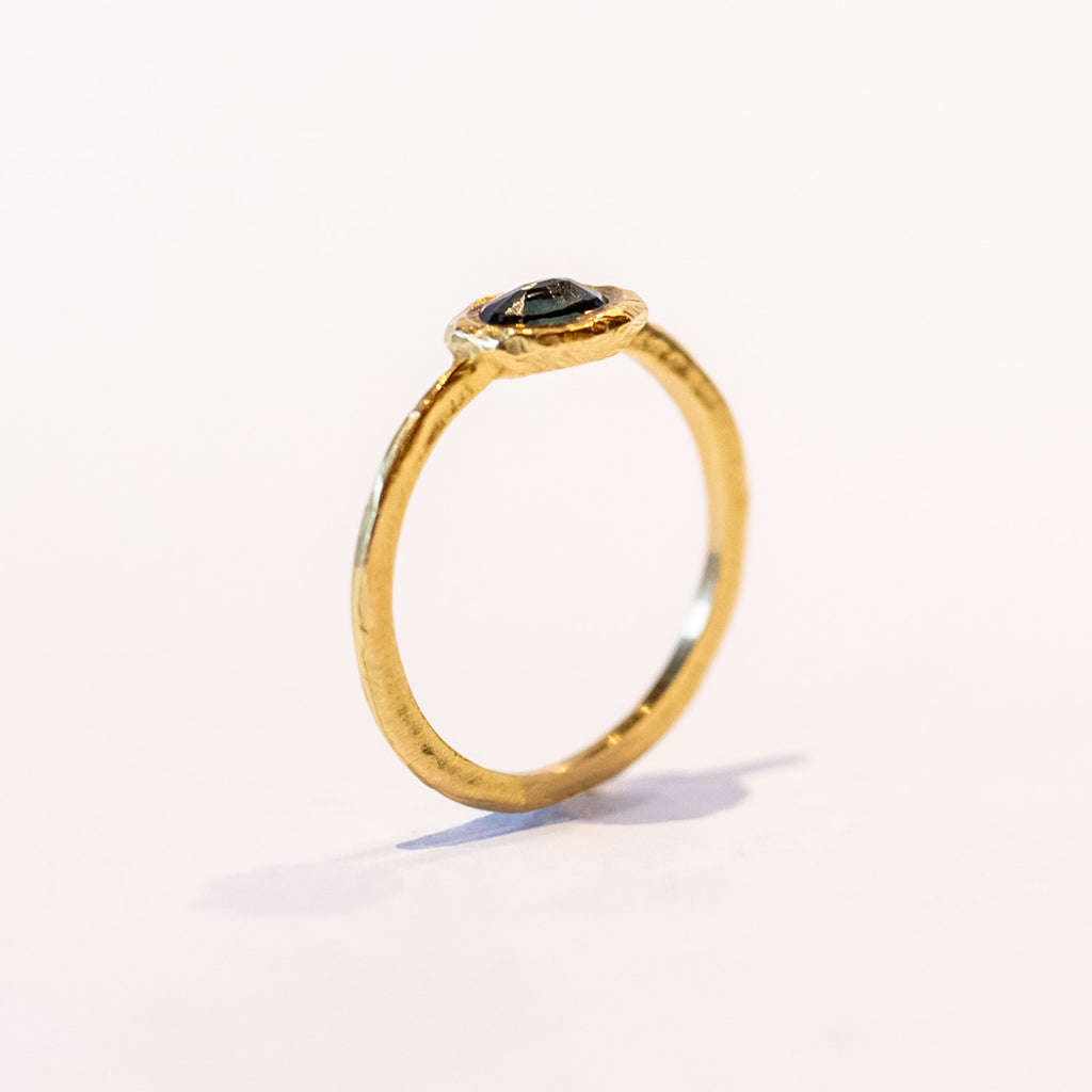 A slender, textured yellow gold ring with an east-west, bezel set teal blue sapphire.