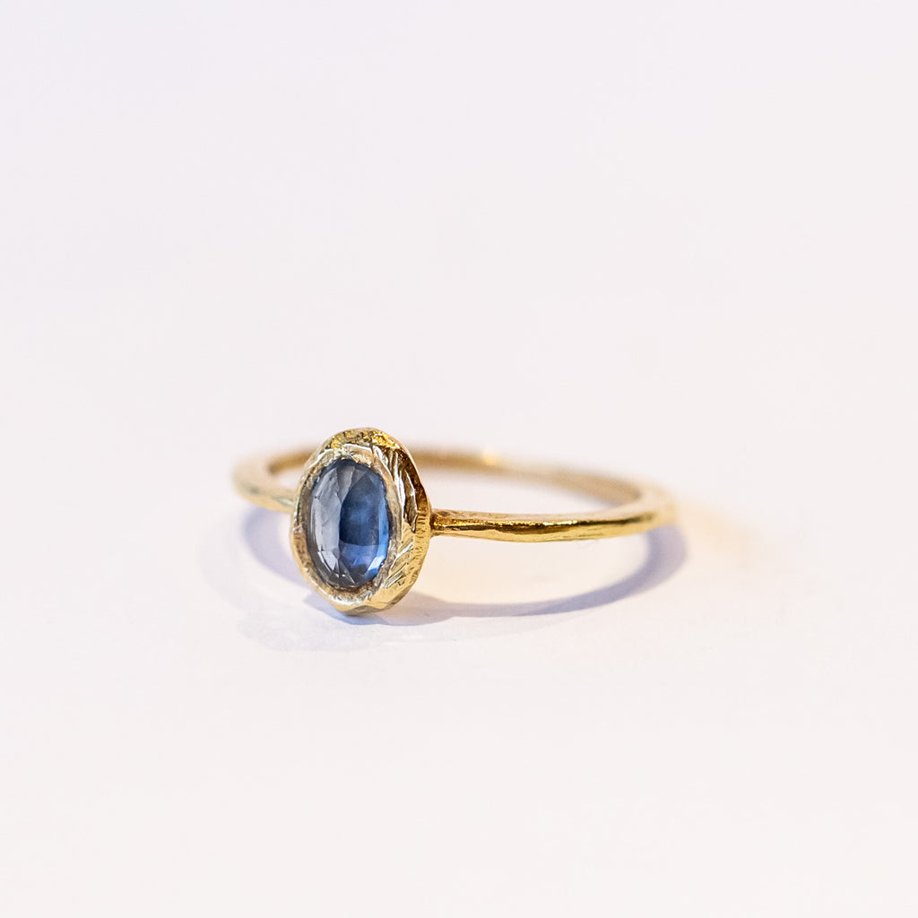 A petite yellow gold ring featuring hand carved texture and a bezel set oval rose cut blue sapphire.