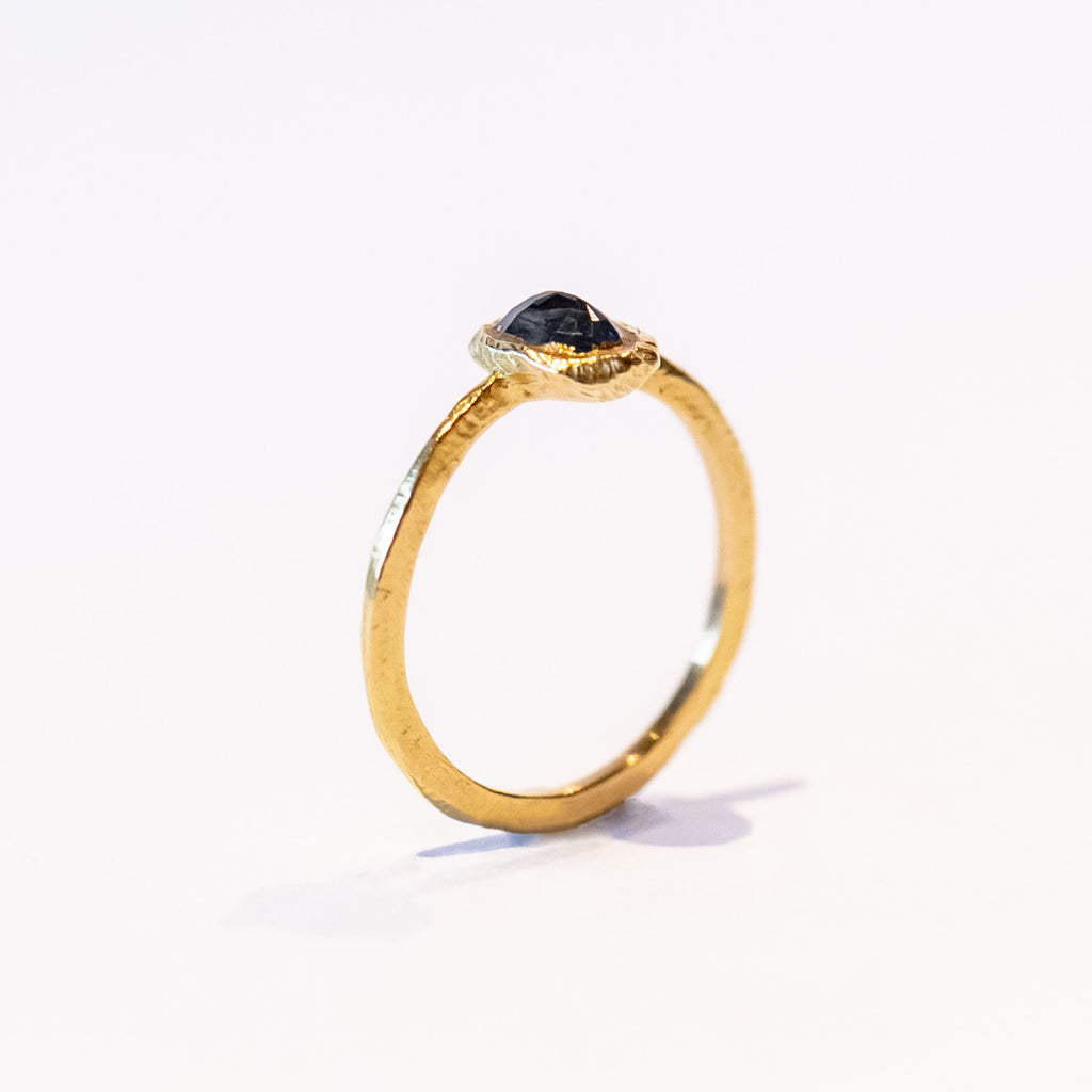 A petite yellow gold ring featuring hand carved texture and a bezel set oval rose cut blue sapphire.