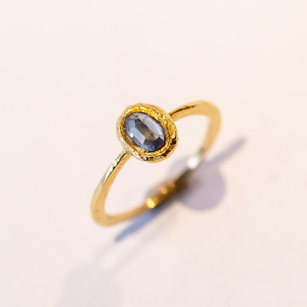A petite yellow gold ring featuring hand carved texture and a bezel set oval rose cut blue sapphire.