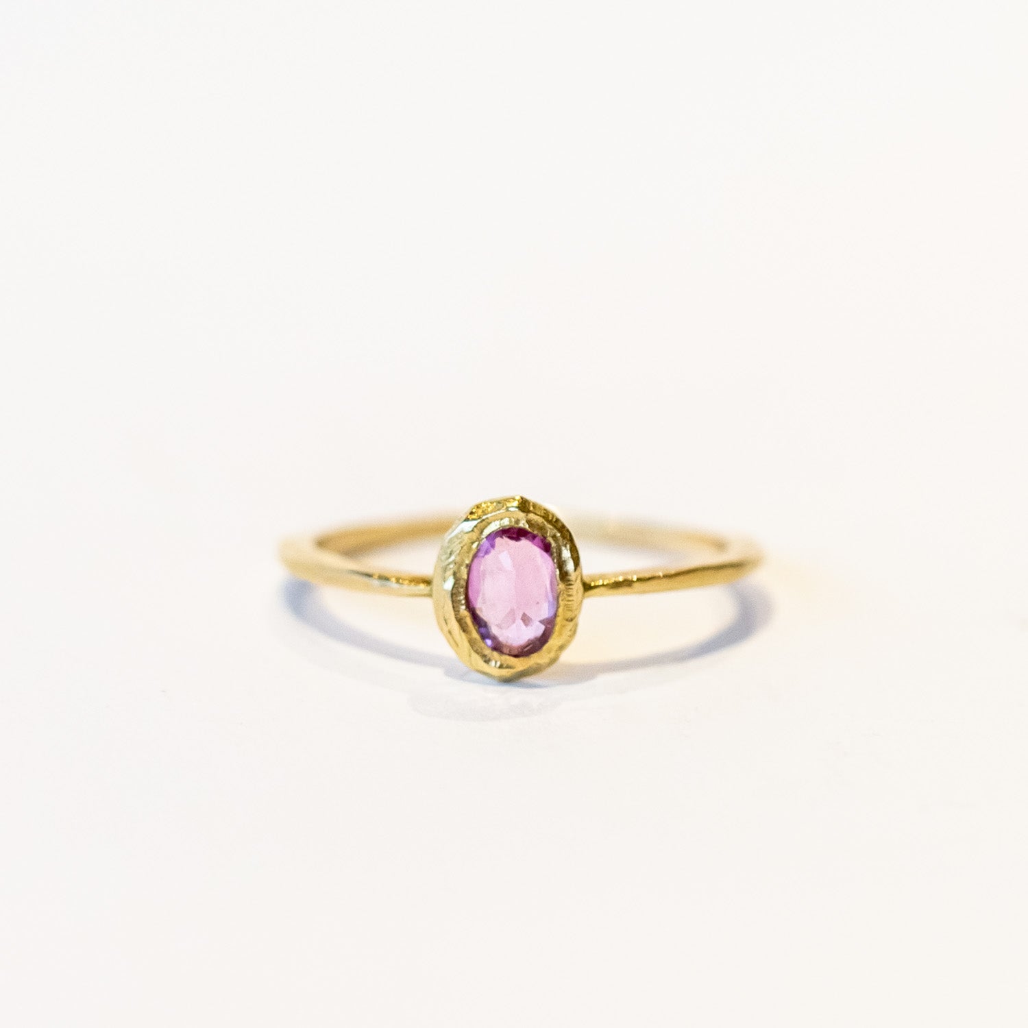 A oval rose cut pink sapphire is set into a textured bezel on a slender yellow gold ring.