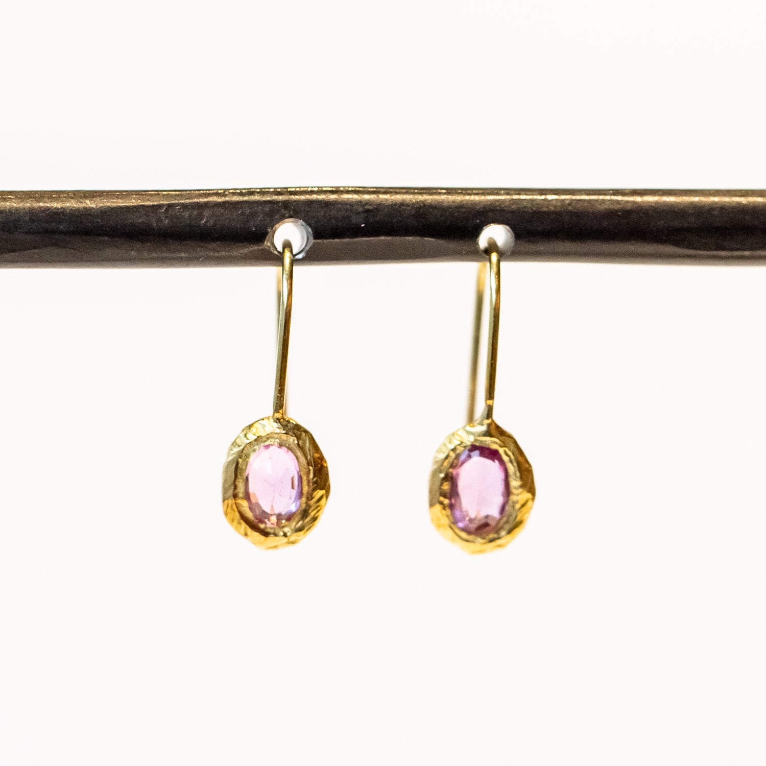 Dainty yellow gold drop earrings featuring oval pink sapphires in textured bezels.