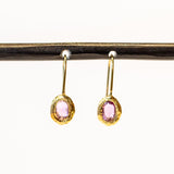 Dainty yellow gold drop earrings featuring oval pink sapphires in textured bezels.