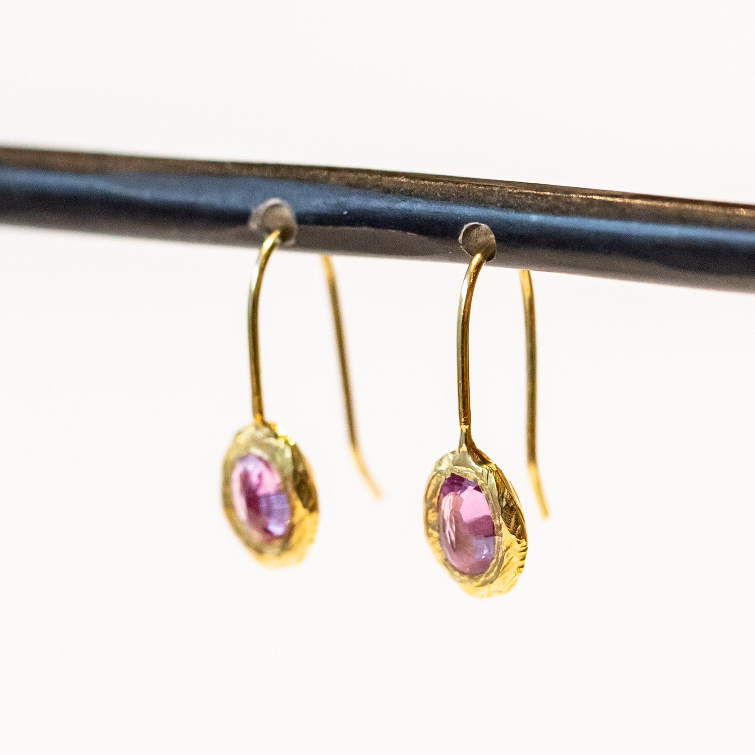 Dainty yellow gold drop earrings featuring oval pink sapphires in textured bezels.