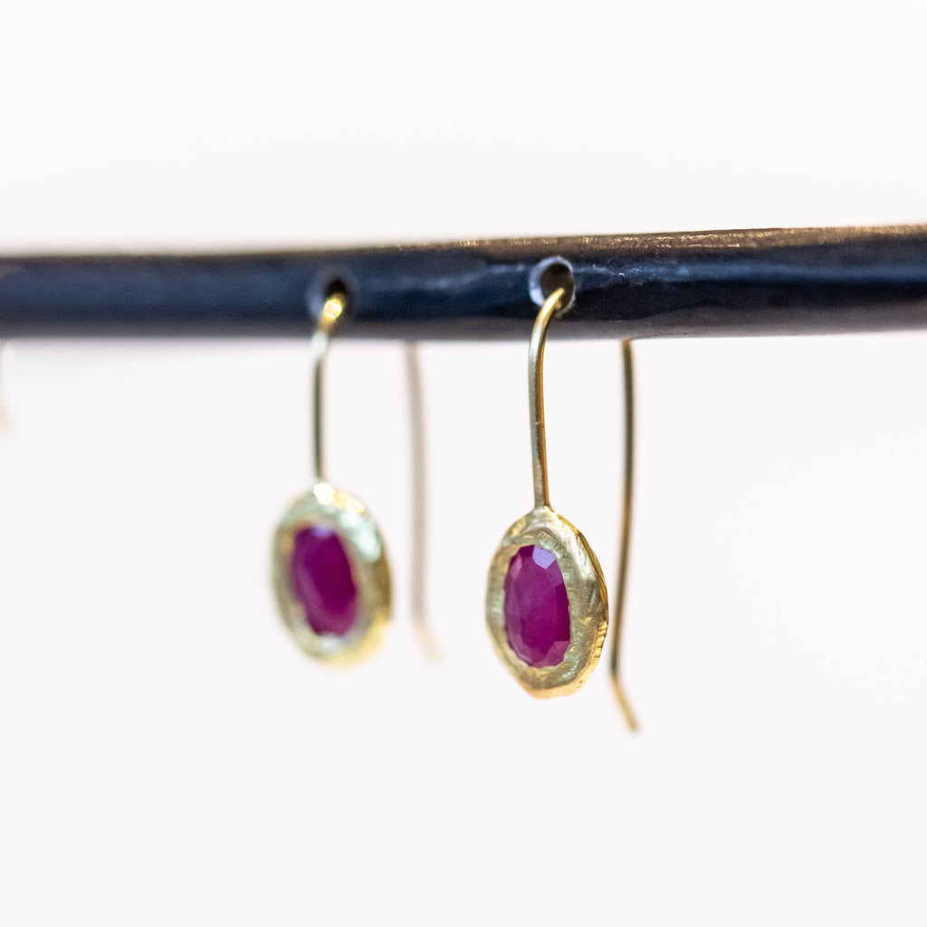 Dainty yellow gold drop earrings with oval rubies set in textured bezels.