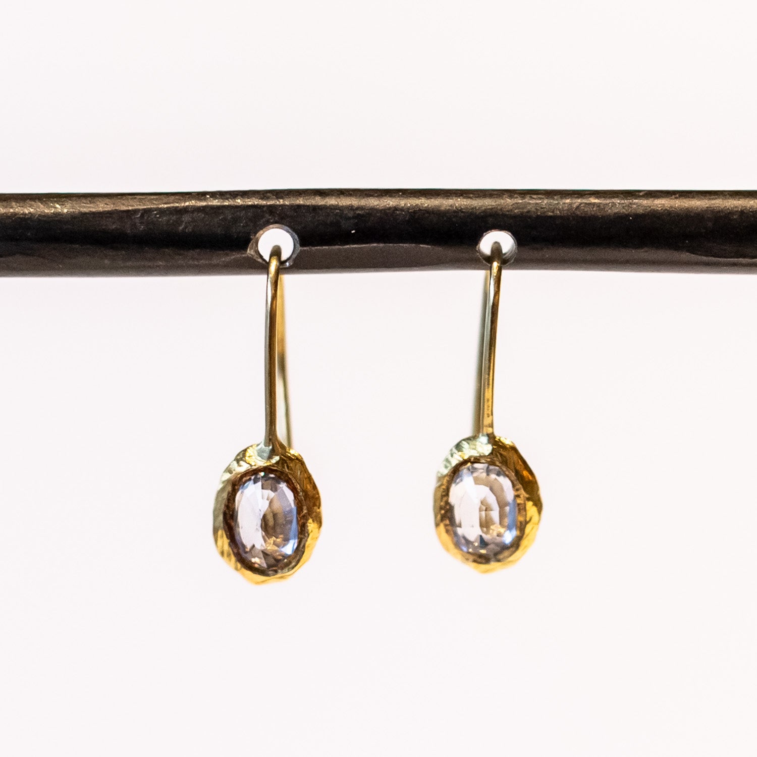 Yellow gold drop earrings with oval blue sapphires set in textured bezels.
