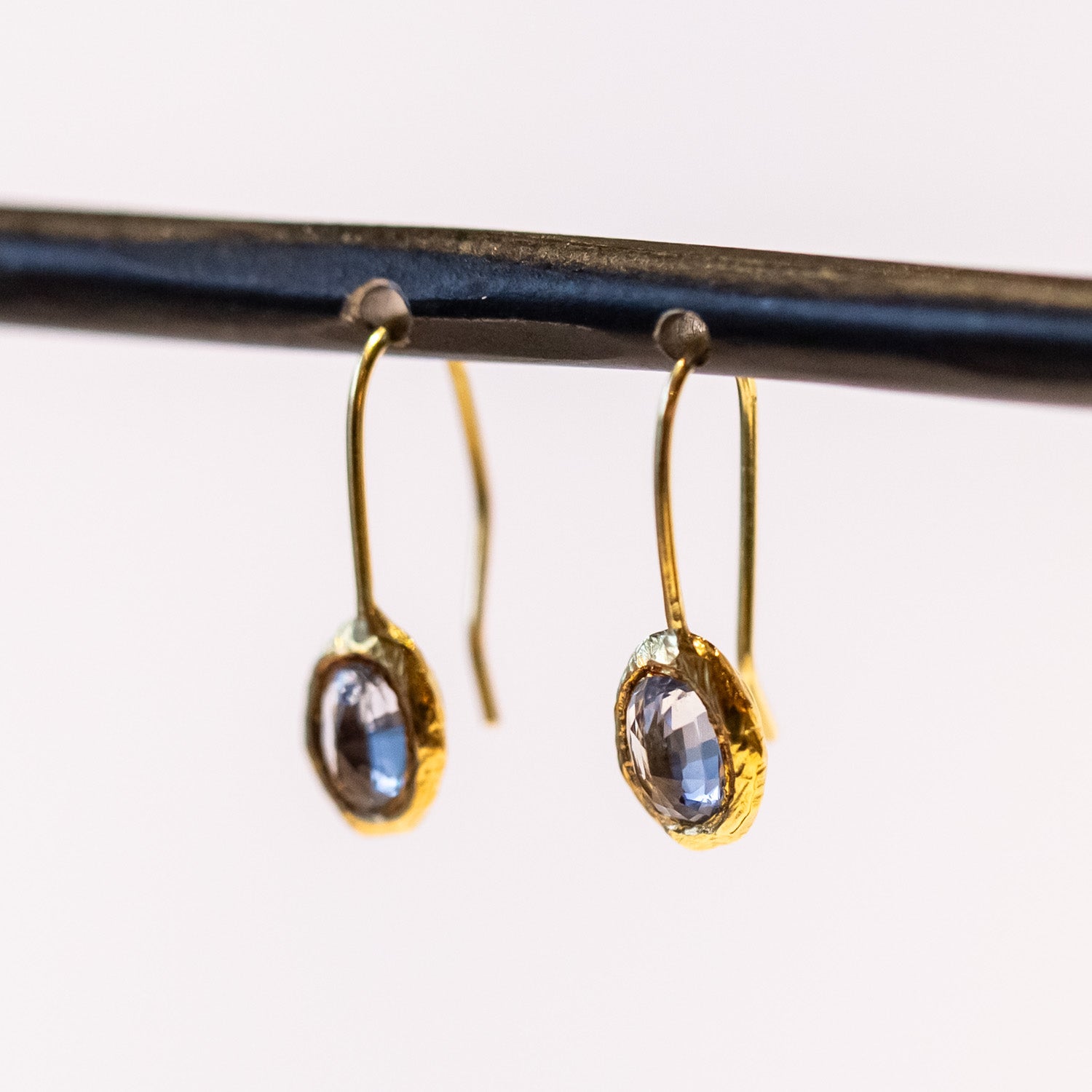 Yellow gold drop earrings with oval blue sapphires set in textured bezels.