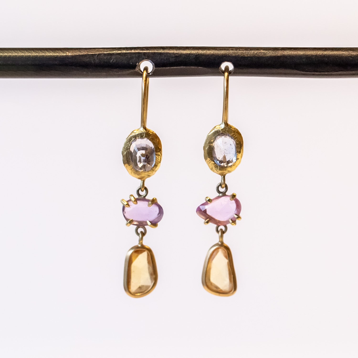 A pair of drop earrings featuring different colored freeform cut sapphires set in different ways in yellow gold.